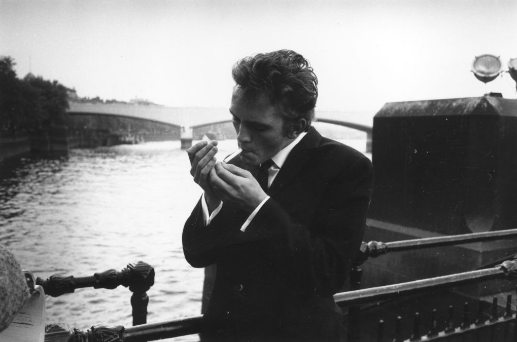 English actor Terence Stamp lighting a cigarette by the river Thames 