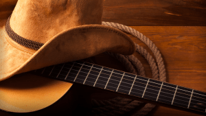 A cowboy hat sitting on top of a guitar laid over coiled rope.