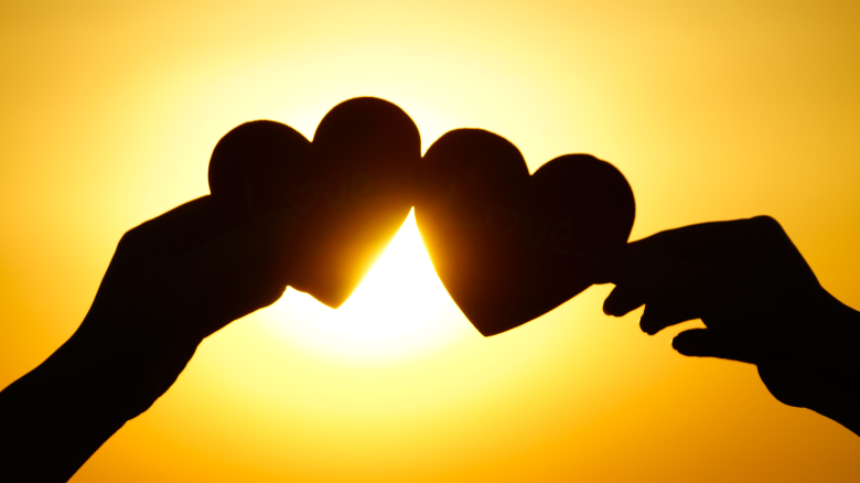 two hands holding two hearts in front of a sunrise