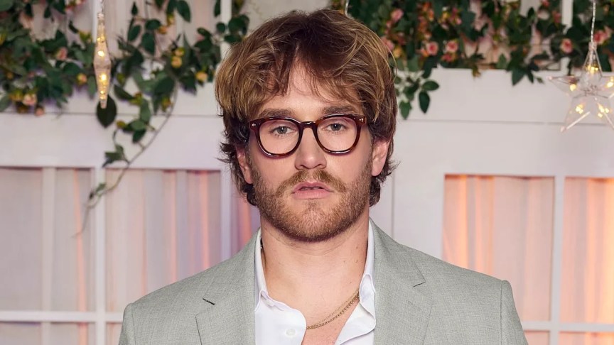 West Wilson poses at a formal event wearing glasses and a light suit