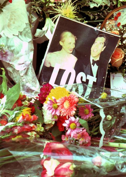 NEW YORK, UNITED STATES: A picture of John F. Kennedy, Jr. and his wife Carolyn Bessette, torn from the front page of a newspaper, sits among the many flowers on the doorstep of the couple's apartment in the Tribeca section of Manhattan 18 July 1999. An intense air and sea search continues off Martha's Vineyard for Kennedy's airplane which disappeared 16 July 1999.