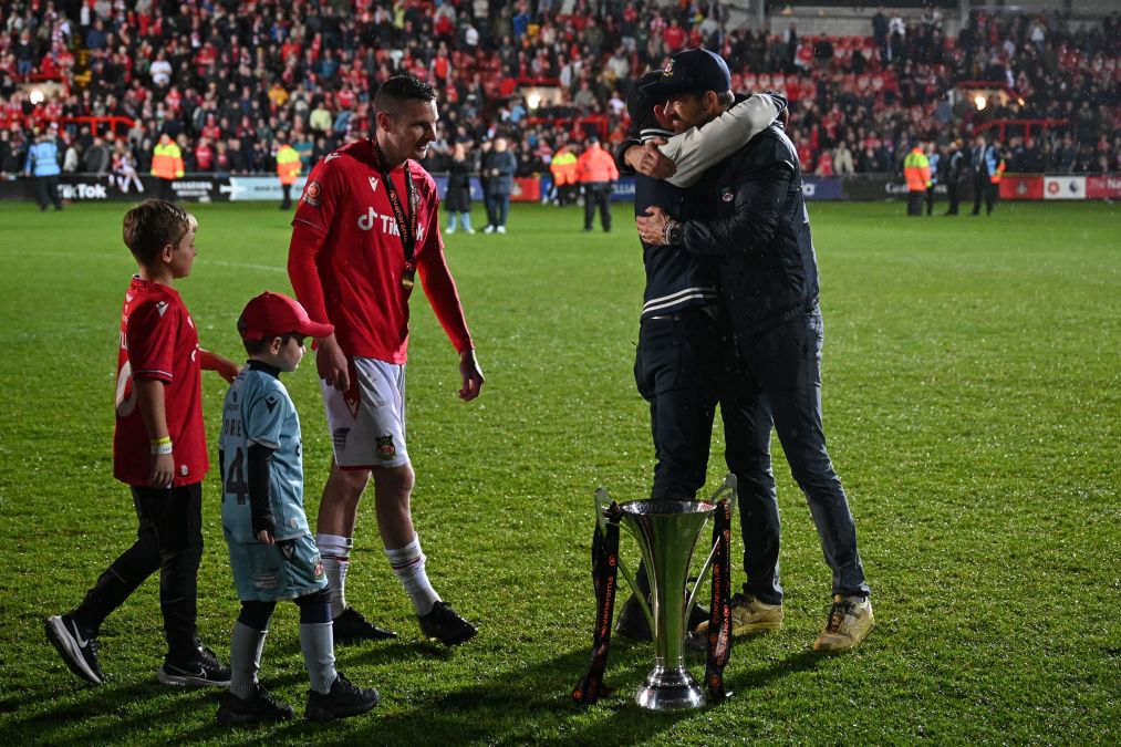 Paul Mullins looks on as Rob McElhenney and Ryan Reynolds embrace.