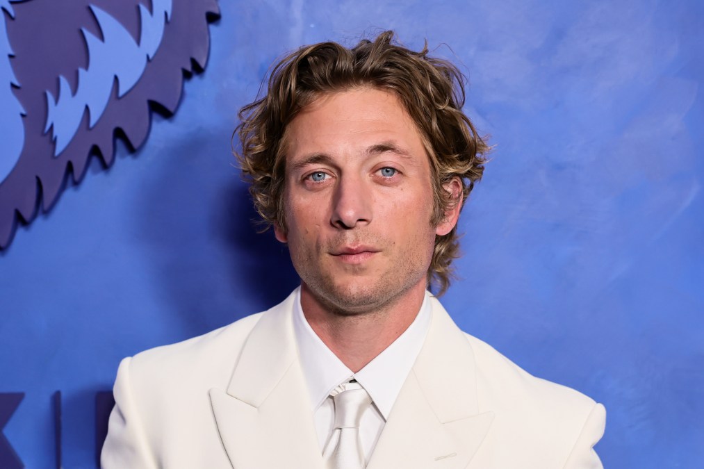 Jeremy Allen White smiling in a dark suit in front of a blue FX step-and-repeat backdrop at the final premiere event.