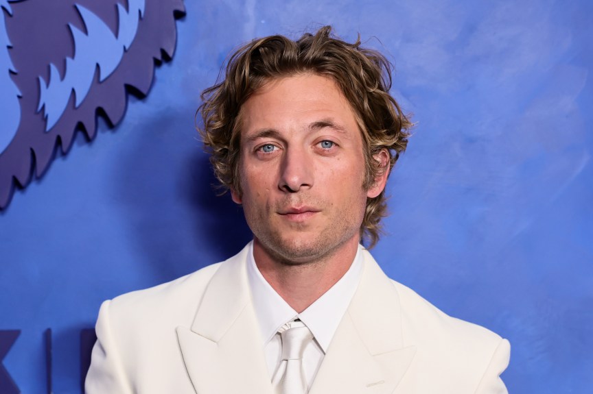 Jeremy Allen White smiling in a dark suit in front of a blue FX step-and-repeat backdrop at the final premiere event.