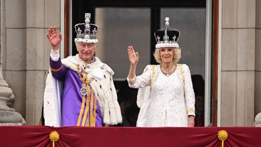 Britain's King Charles III wearing the Imperial state Crown, and Britain's Queen Camilla wearing a modified version of Queen Mary's Crown wave from the Buckingham Palace balcony after viewing the Royal Air Force fly-past in central London on May 6, 2023