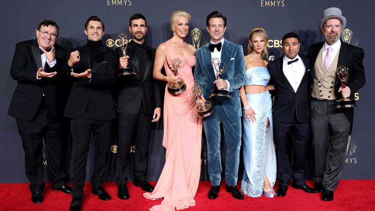 Members of the "Ted Lasso" cast pose together with Emmy Awards on the red carpet.