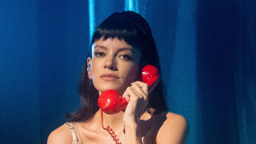 Lily Allen performing on the stage with a phone to her ear