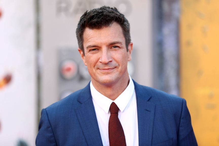Nathan Fillion smiles in blue suit and maroon tie