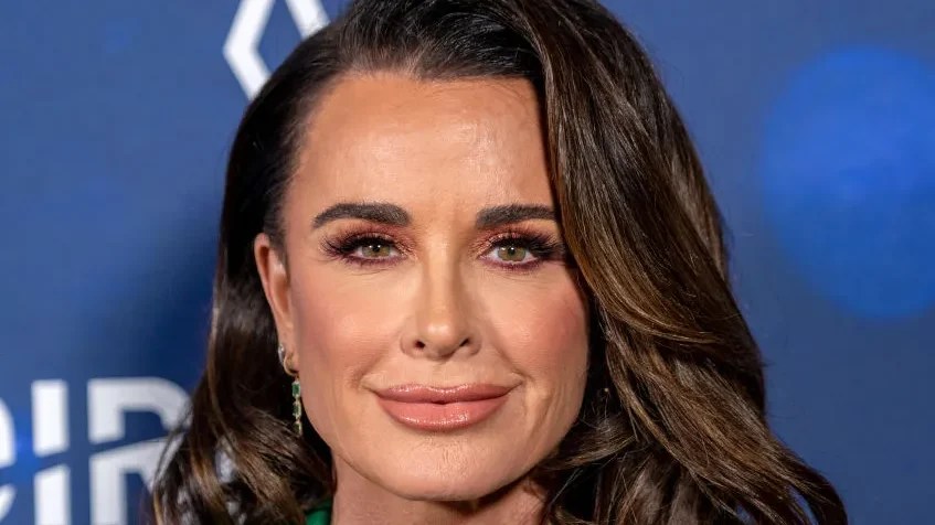 Kyle Richards poses for a portrait while wearing an emerald green suit and layered green gemstone necklaces at a red carpet event.