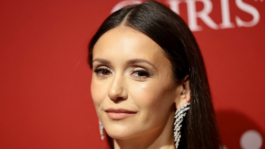 Nina Dobrev looks at the camera and wears long earrings.