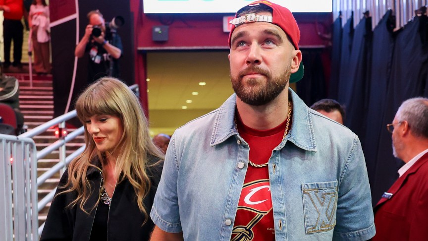 Taylor Swift and Travis Kelce walk through a stadium holding hands.