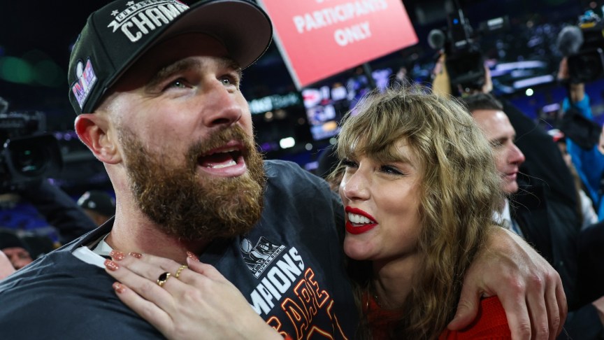 Taylor Swift looks up at Travis Kelce on a football field.