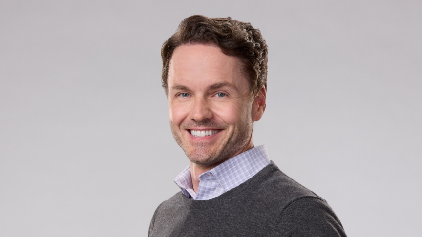 Paul Campbell smiles in sweater and white button down shirt
