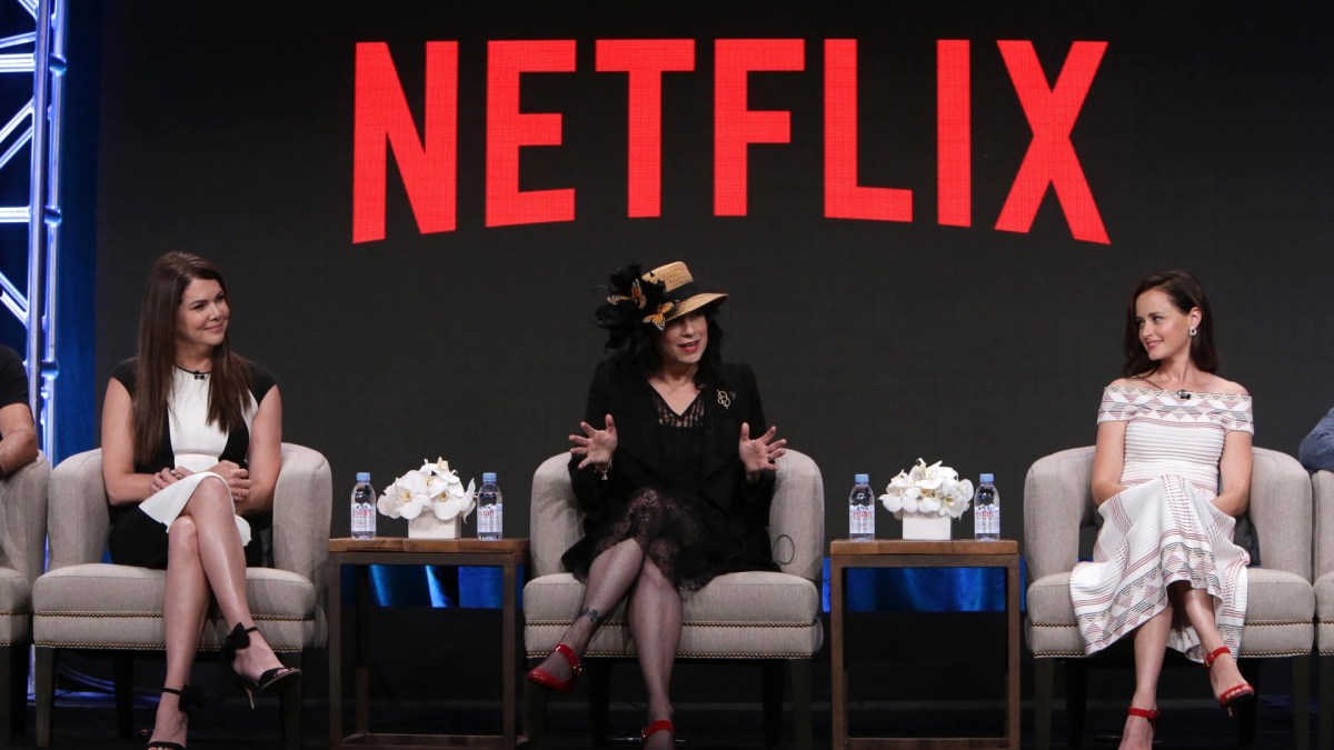 Lauren Graham, Amy Sherman-Palladino, and Alexis Bledel sits in love seats on stage under a Netflix sign.